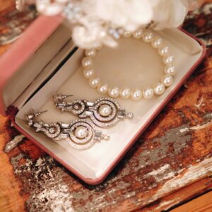 A close-up of luxurious pearls and intricate earrings in an open jewelry box on a rustic wooden table.